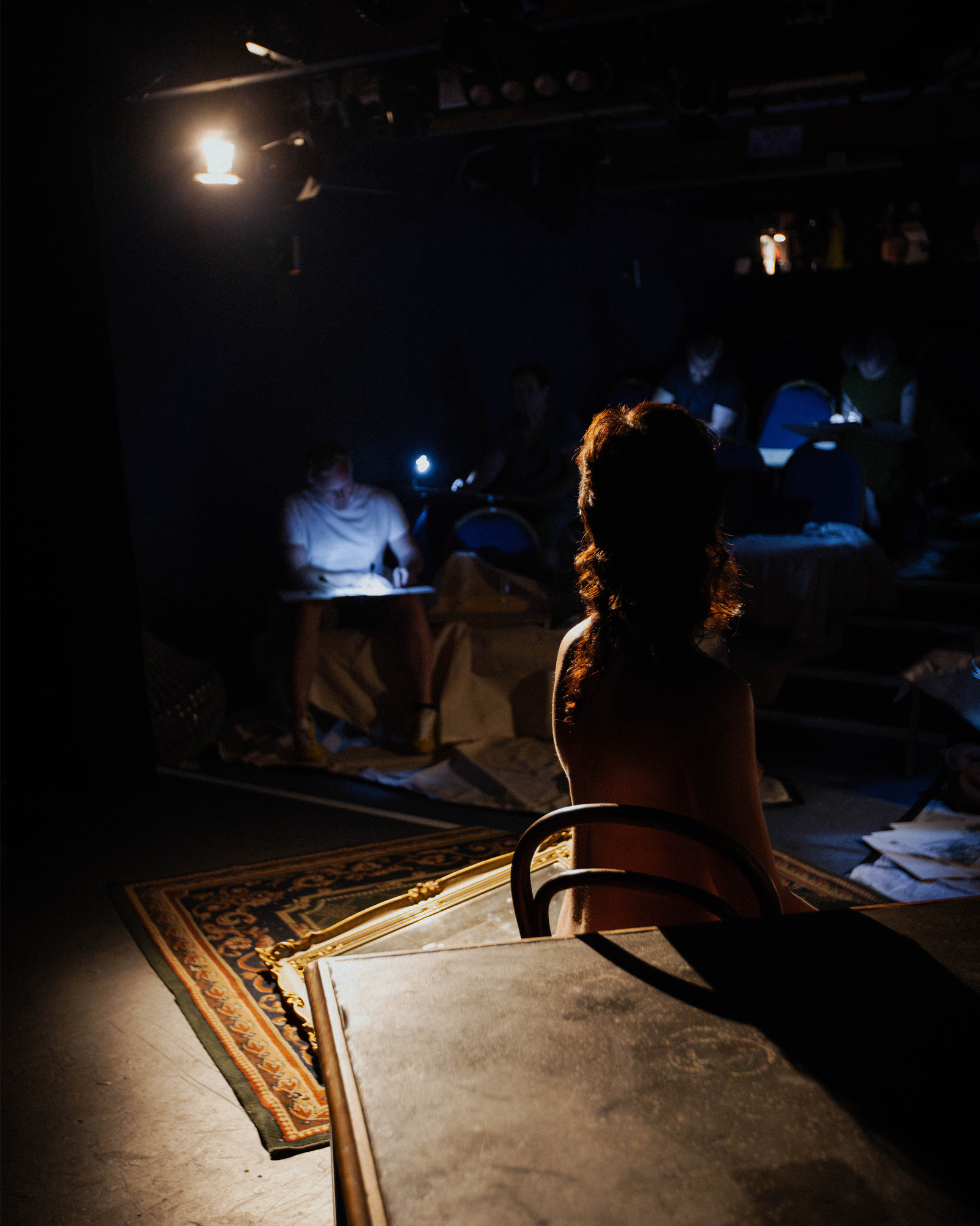 Performer seen from behind facing an audience drawing under theatrical lighting at Theatre Life Drawing.